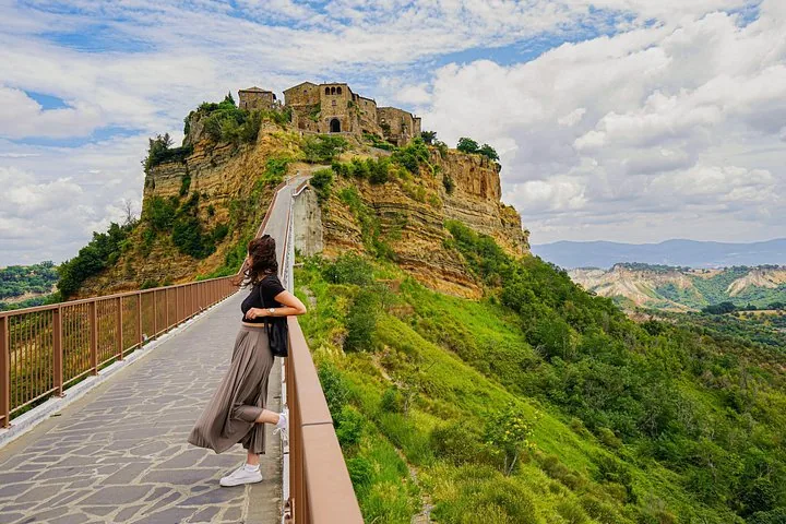 A visitor on the footbridge to Civita di Bagnoregio, with railings on both sides and the village above